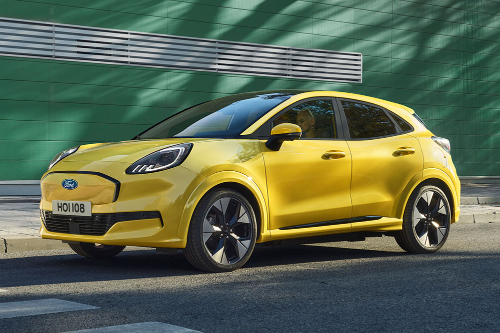 Zółty Ford Puma Gen-E zaparkowany na przed zielonym budynkiem.