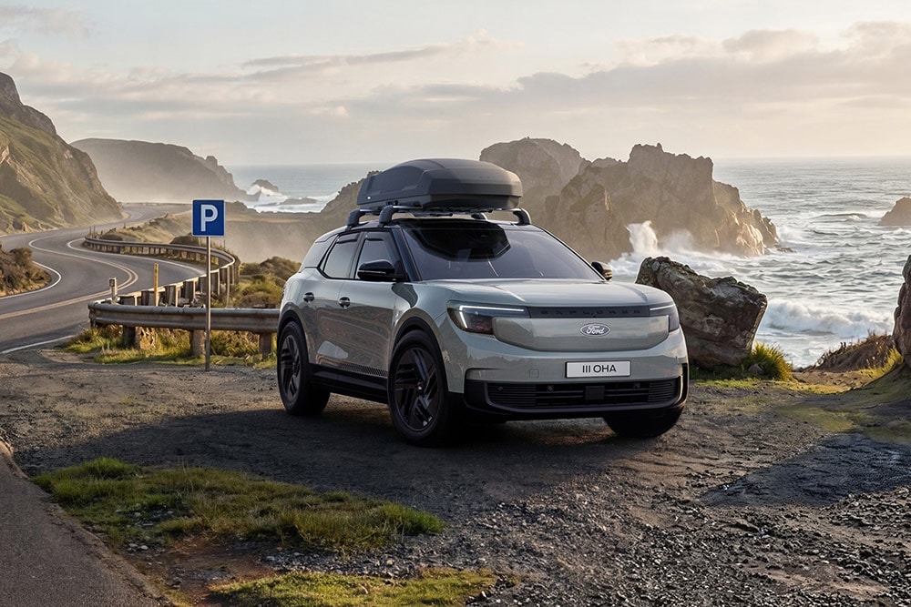 Szary Ford Explorer z bagażnikiem dachowym, zaparkowany na nadmorskiej drodze. 