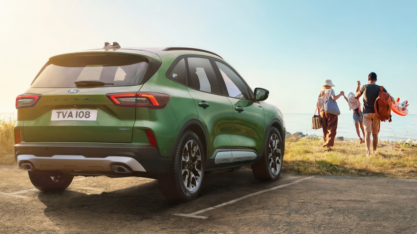 Zielony Ford SUV zaparkowany nad morzem, obok rodzina idąca w stronę plaży w słoneczny dzień.