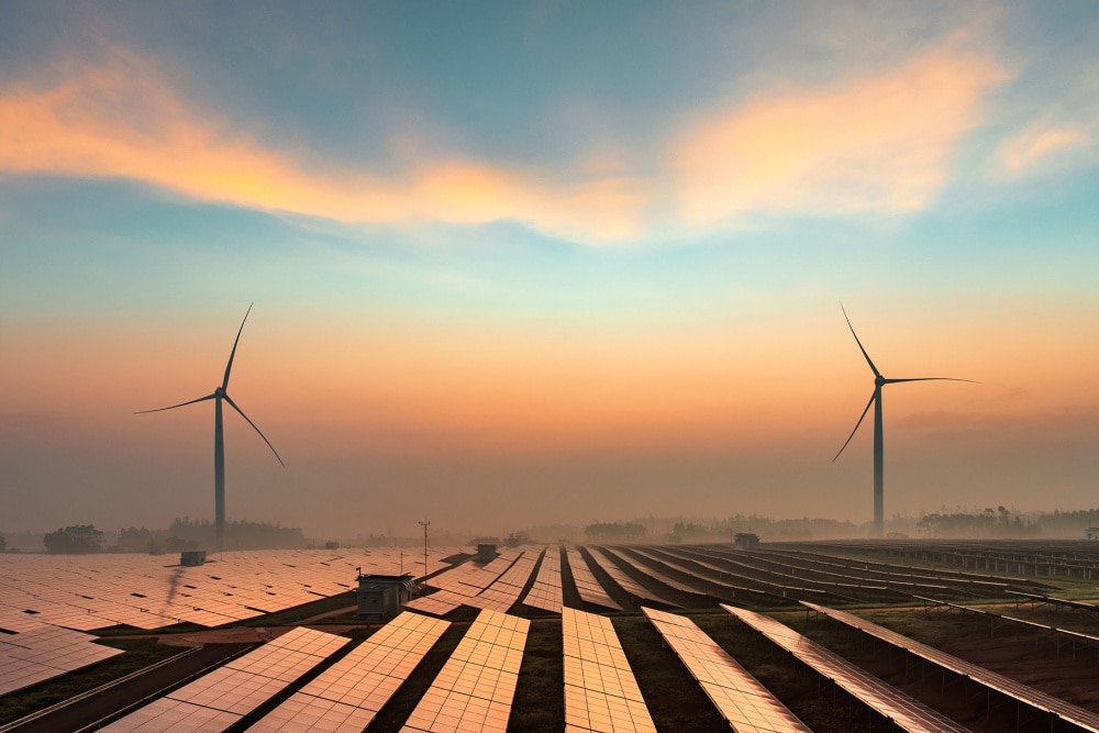 Odnawialne źródła energii, w tym turbiny wiatrowe i panele słoneczne, przedstawione na tle zachodzącego słońca.