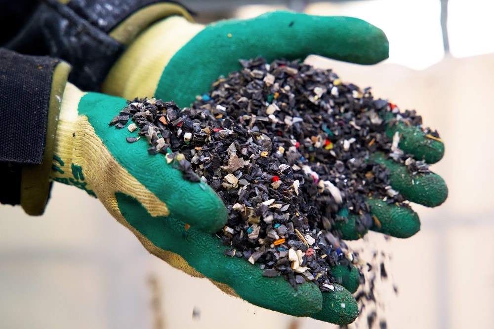 Dłonie w gumowych rękawicach trzymające kawałki plastikowych odpadów przeznaczonych do recyklingu.