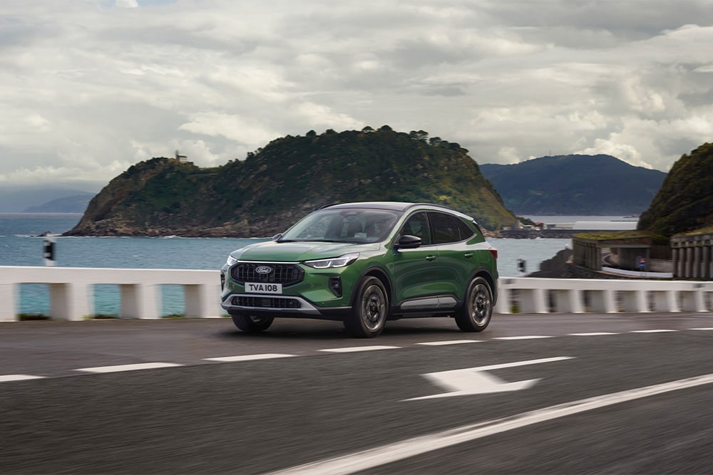 Zielony Ford Kuga z napędem full hybrid jadący po malowniczej drodze.