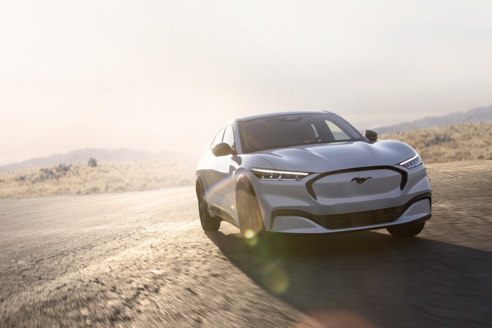 Srebrny elektryczny Ford Mustang Mach-E GT jadący po malowniczej drodze.