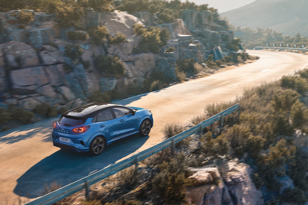 Niebieski Ford Puma Gen-E jadący krętą górską drogą.