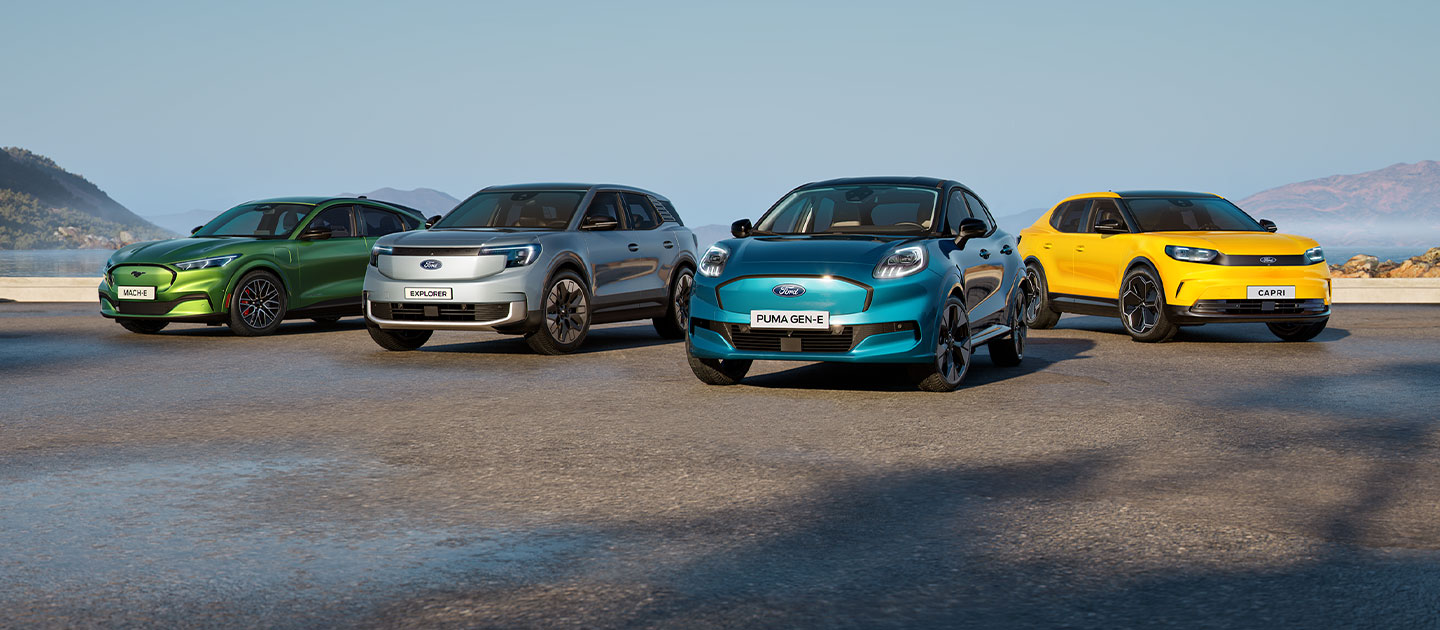 Różne pojazdy elektryczne Forda zaparkowane na tle surowego nadmorskiego krajobrazu.