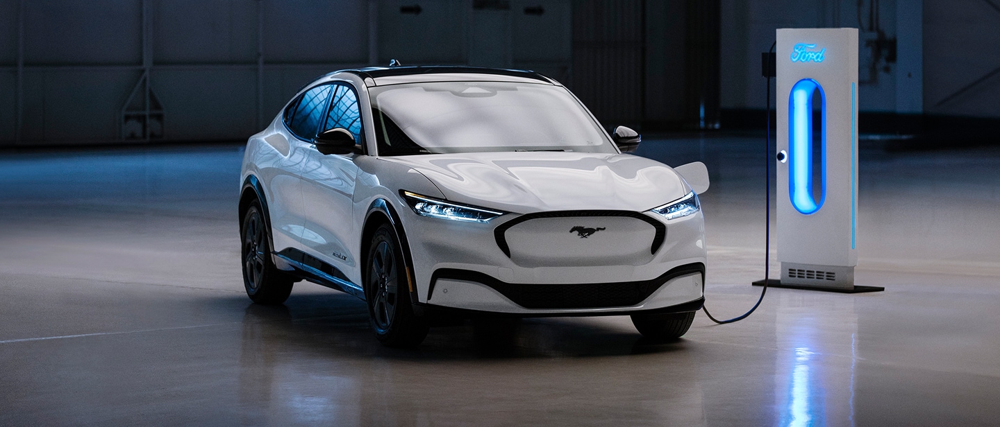 Biały Ford Mustang Mach-E podłączony do podświetlonej na niebiesko stacji ładowania w garażu.