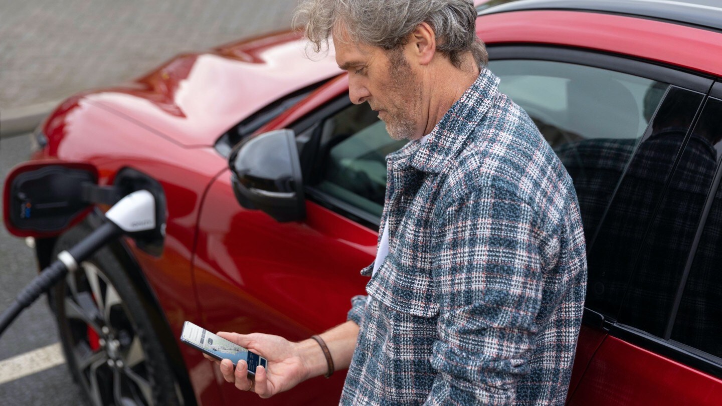 A man looking at a smartphone while charging a car