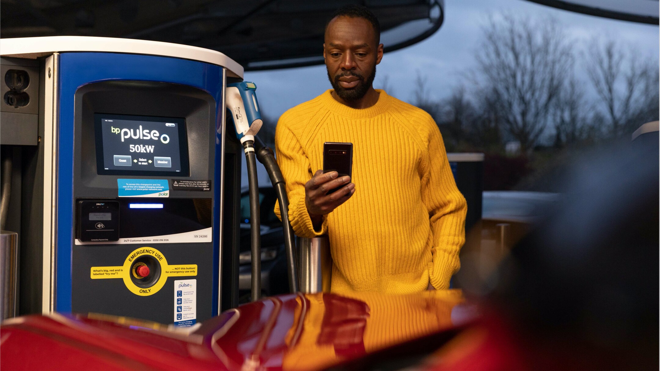 A man looking at a smartphone next to a Mustang Mach-E