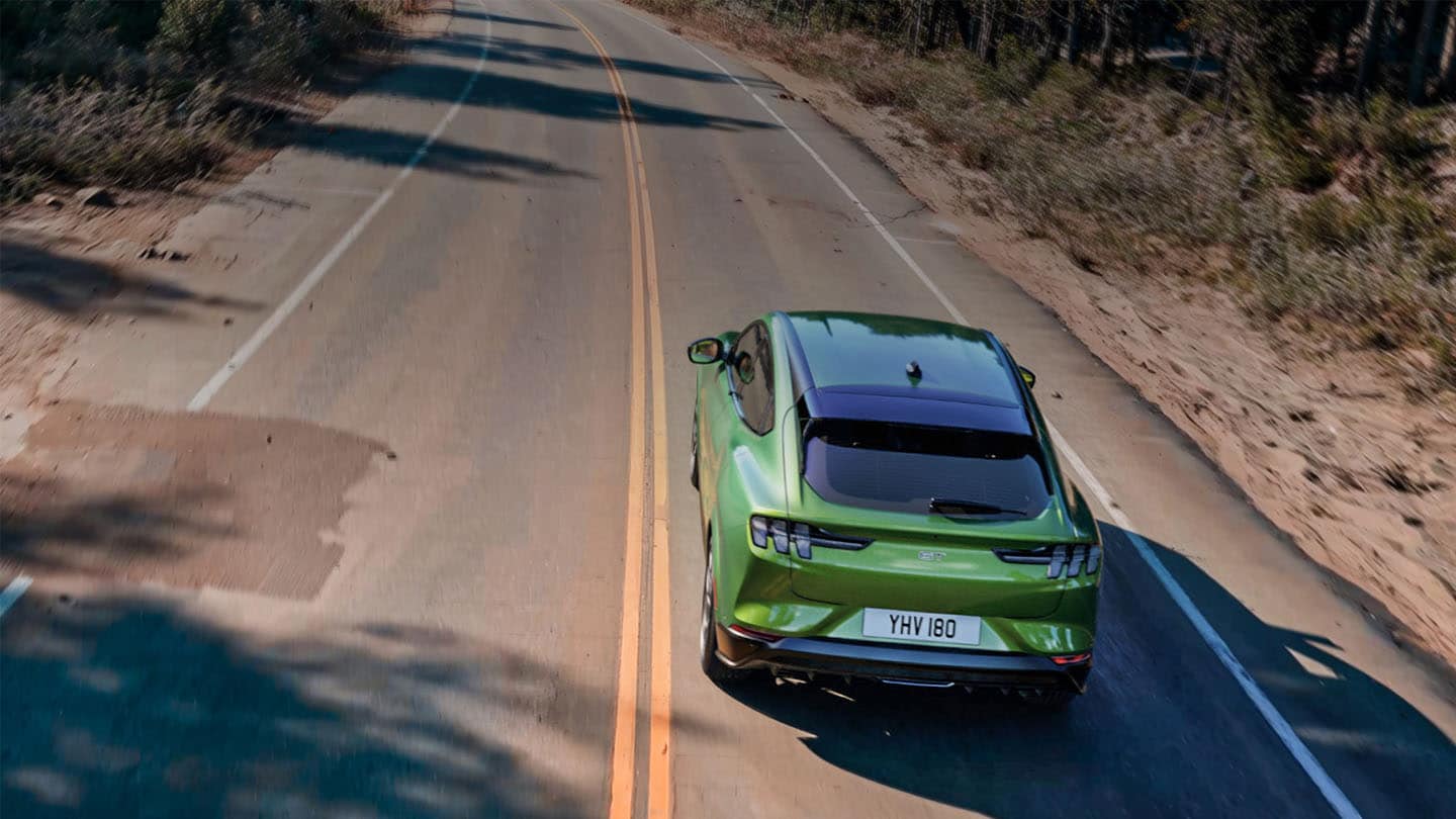 Ford Mustang Mach-E GT w kolorze Eruption Green pokonuje górską drogę wśród drzew.