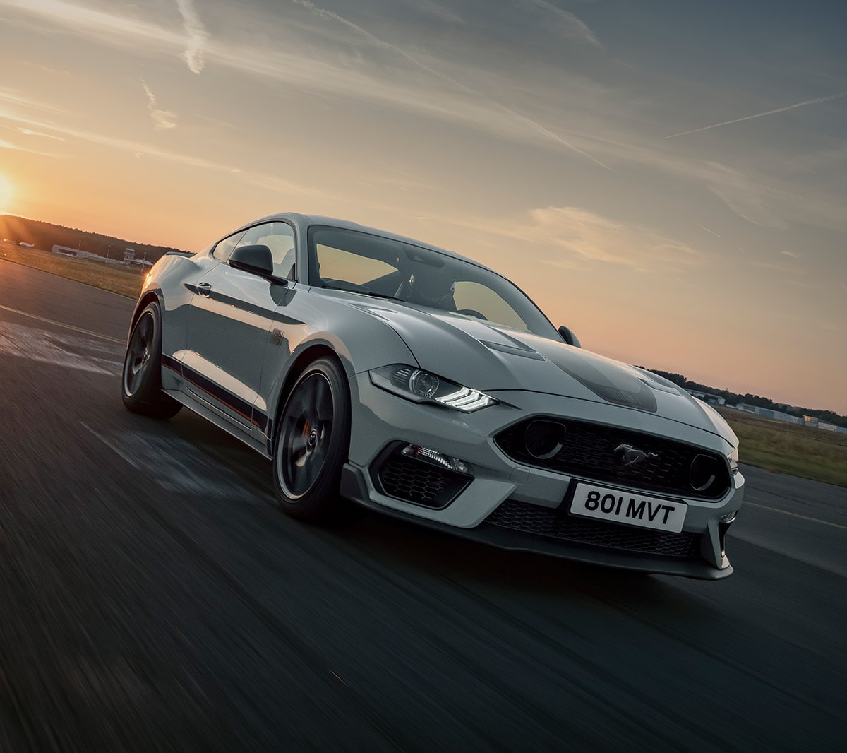 Ford Mustang Mach 1 drving on a racetrack against a sunset backdrop.