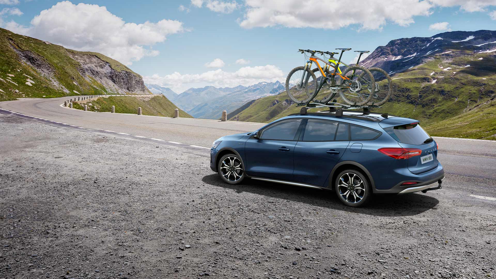 Niebieski Ford Focus z rowerami na dachu jadący malowniczą górską drogą.