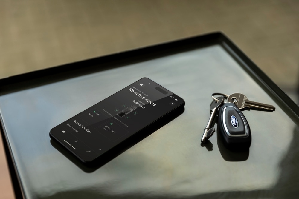 Smartfon wyświetlający aplikację Ford App ze stanem pojazdu, leżący obok kluczyka do Forda.