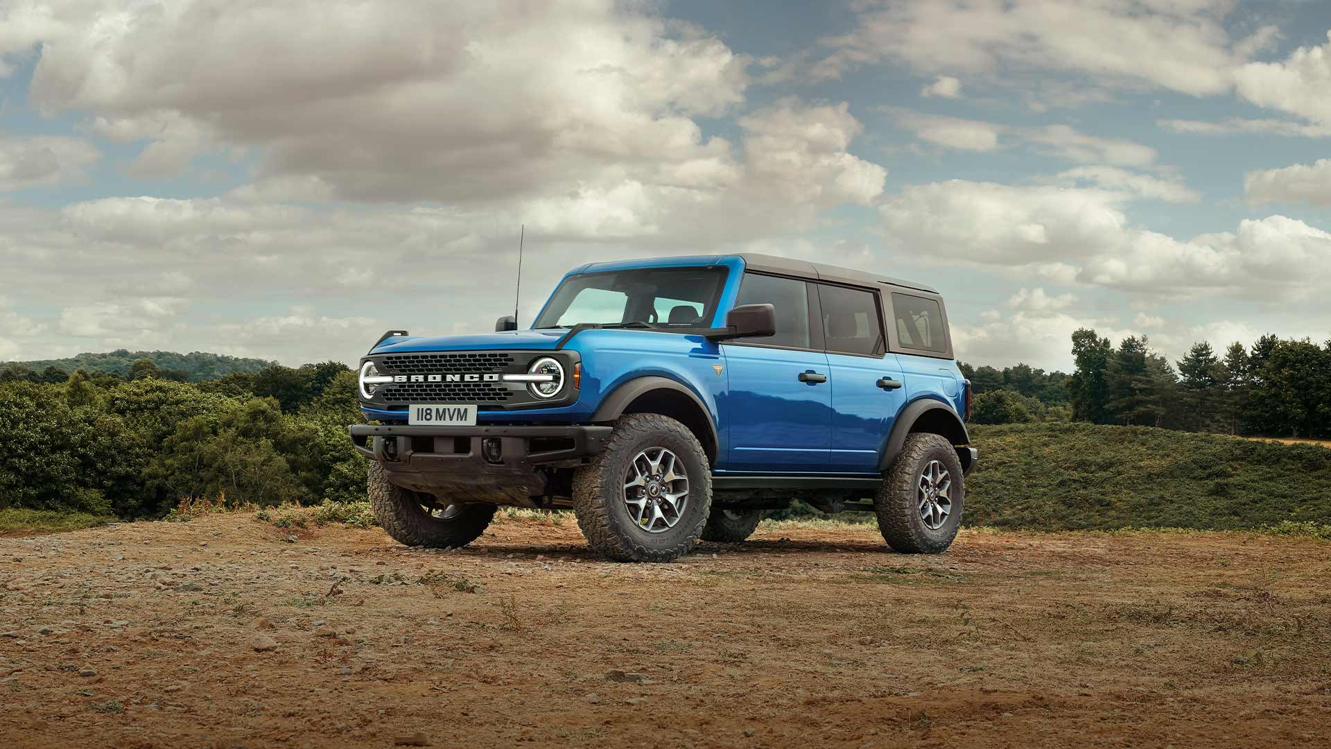Widok z boku niebieskiego Forda Bronco zaparkowanego w wiejskim otoczeniu.