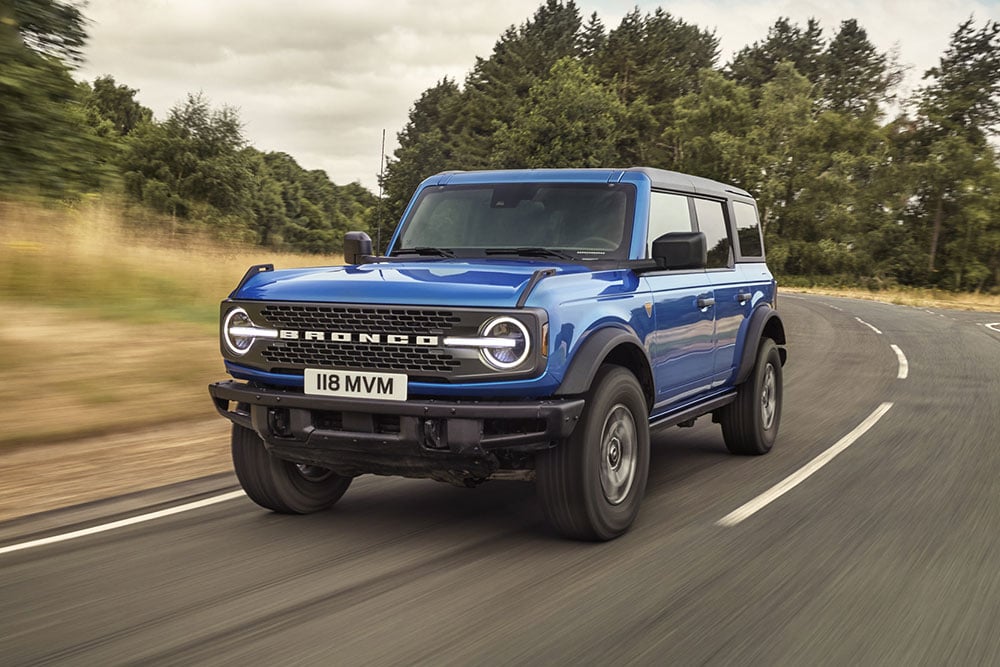 Widok z przodu nowego Forda Bronco w kolorze niebieskim podczas jazdy wiejską drogą.