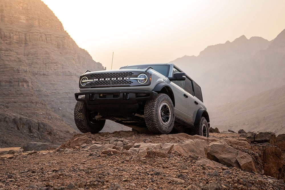 Szary Ford Bronco zaparkowany na skalistej ścieżce w górzystym krajobrazie.