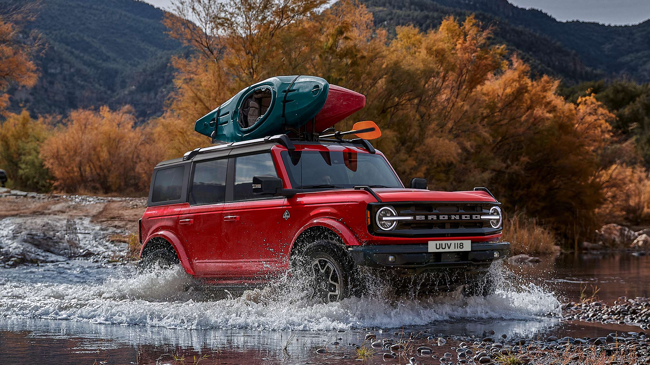 Ford Bronco driving through a small lake in the mountains with kayaks attached to the roof