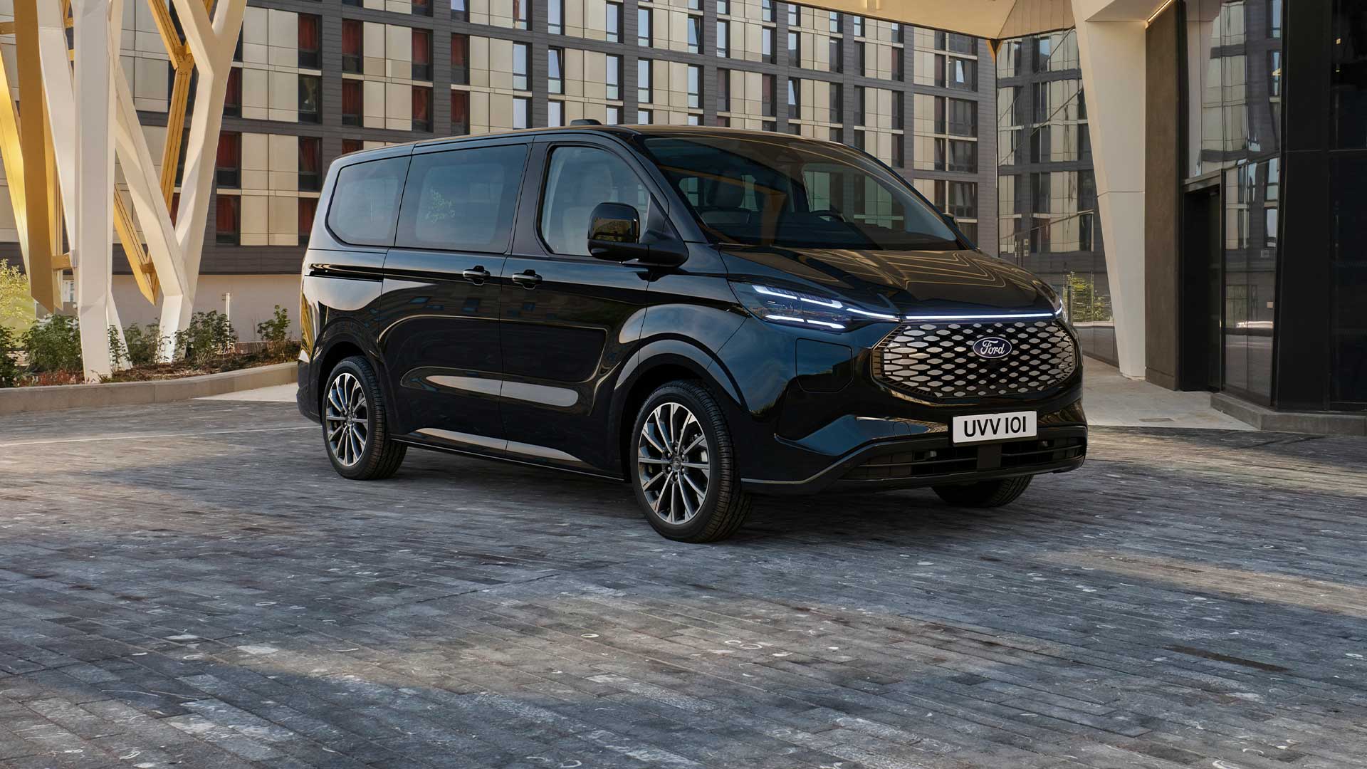 Czarny Ford E-Tourneo Custom stoi przed nowoczesnym budynkiem.