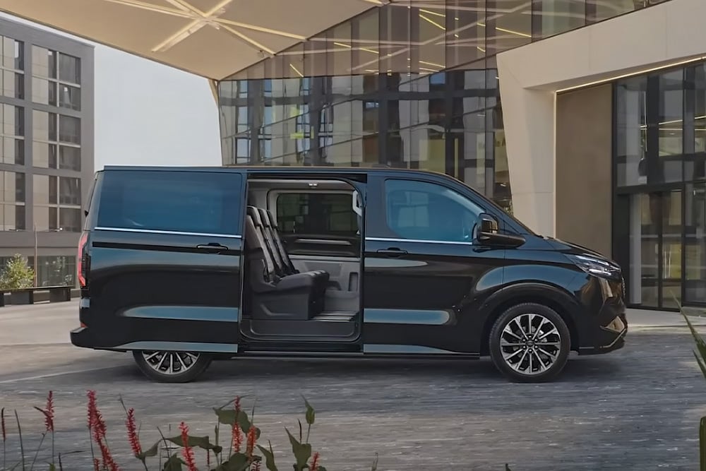 Czarny Ford E-Tourneo Custom jest zaparkowany z otwartymi drzwiami bocznymi, ukazując fotele we wnętrzu.