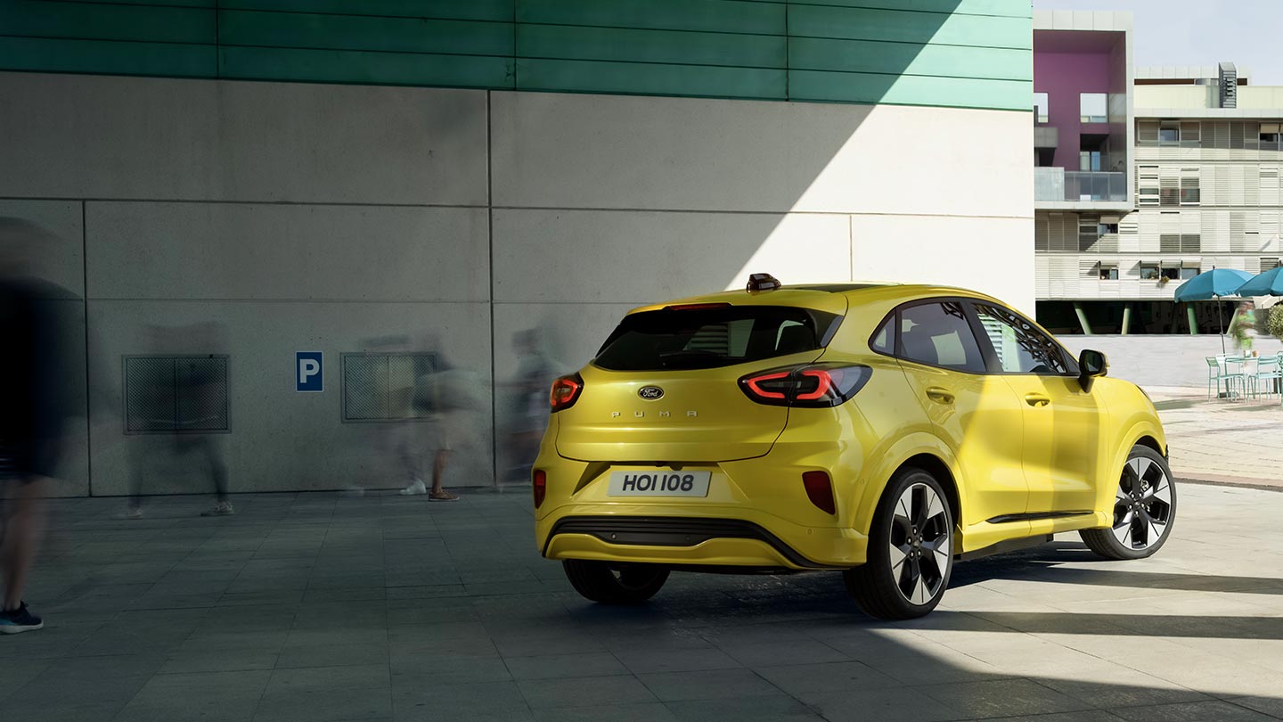 Widok z tyłu pod kątem na żółtego elektrycznego Forda Puma Gen-E® zaparkowanego pod mostem.