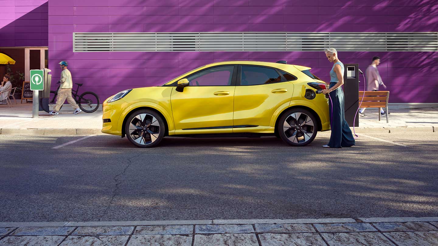 Widok z boku na żółtego elektrycznego Forda Puma Gen-E® podłączanego do publicznej stacji ładowania na parkingu.