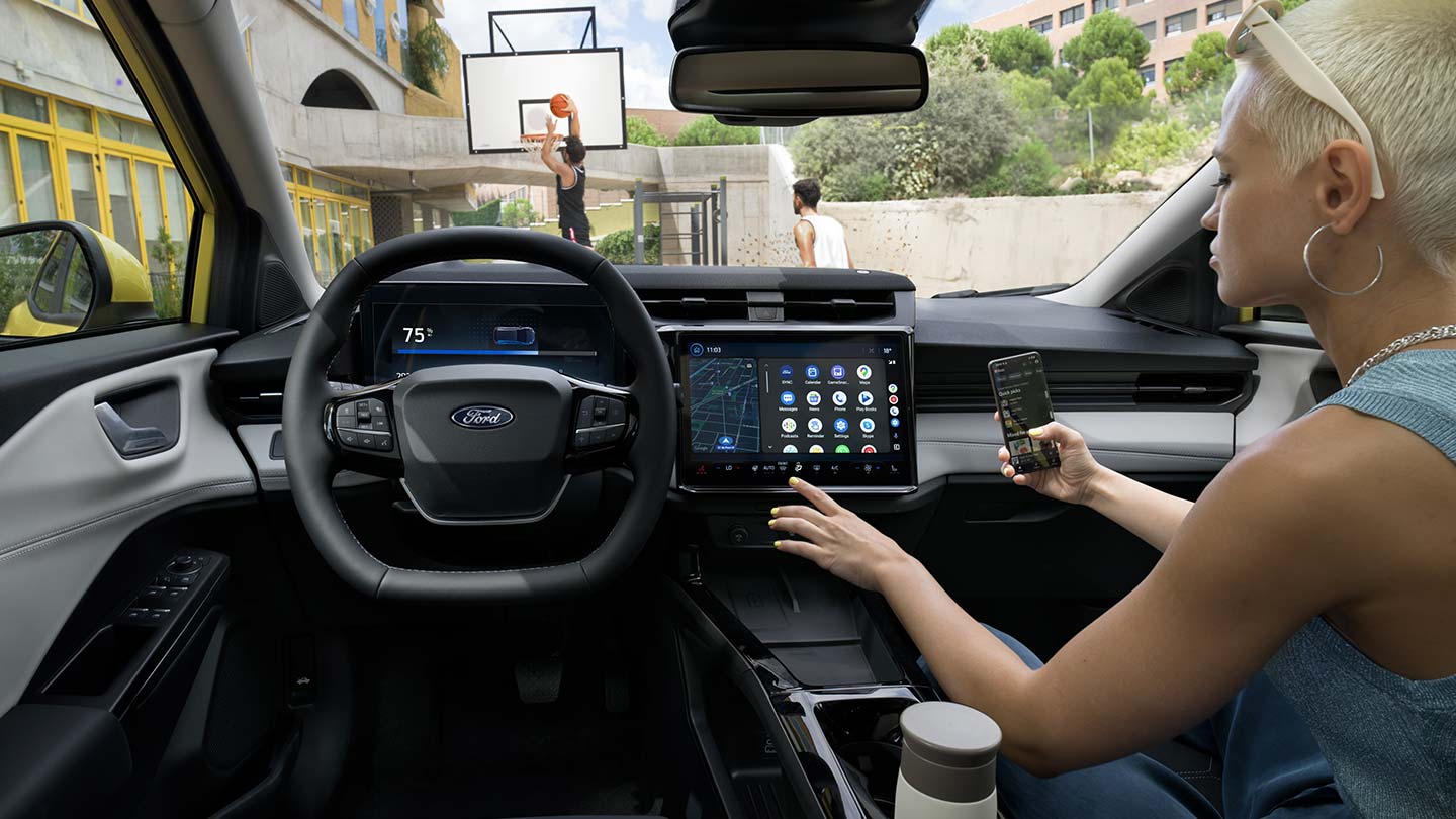 Wnętrze elektrycznego Forda Puma Gen-E® i osoba bezprzewodowo synchronizującą telefon komórkowy z dużym ekranem dotykowym.