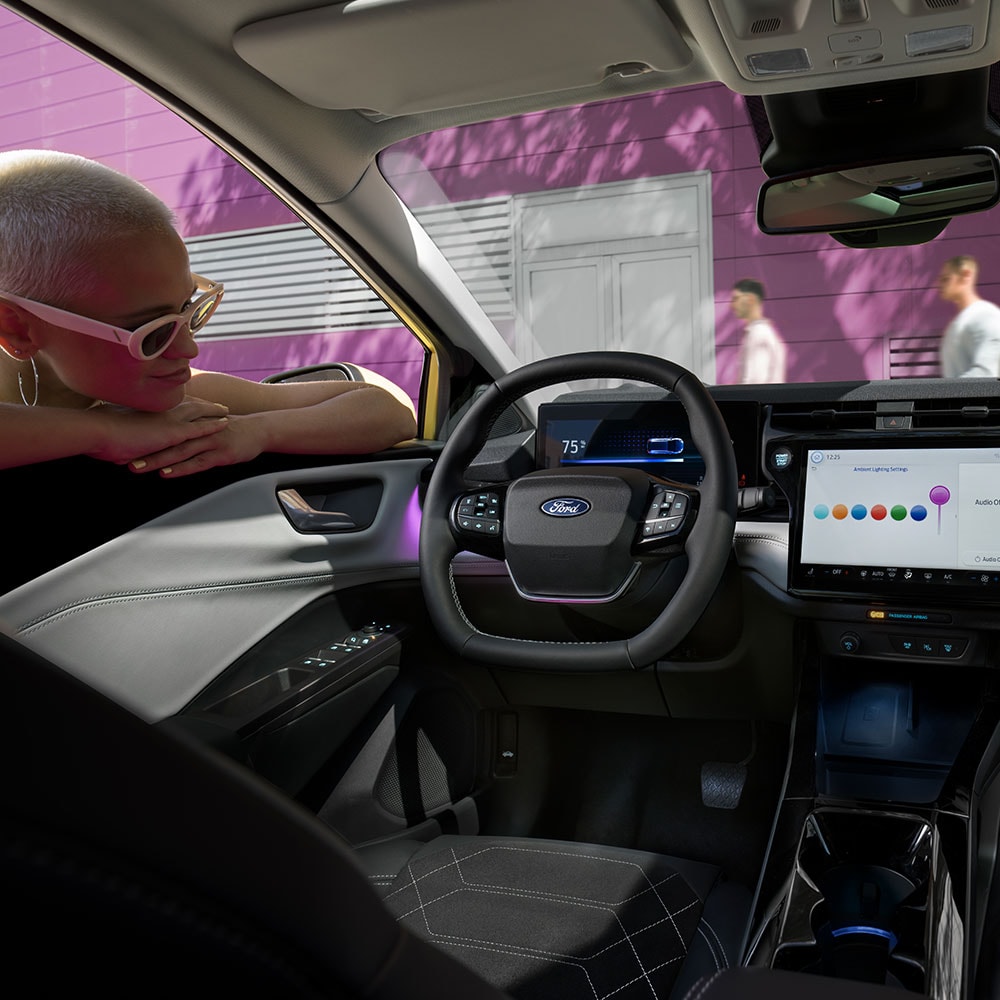 Wnętrze elektrycznego Forda Puma Gen-E®, z osobą patrzącą przez szybę na duży ekran systemu inforozrywki.