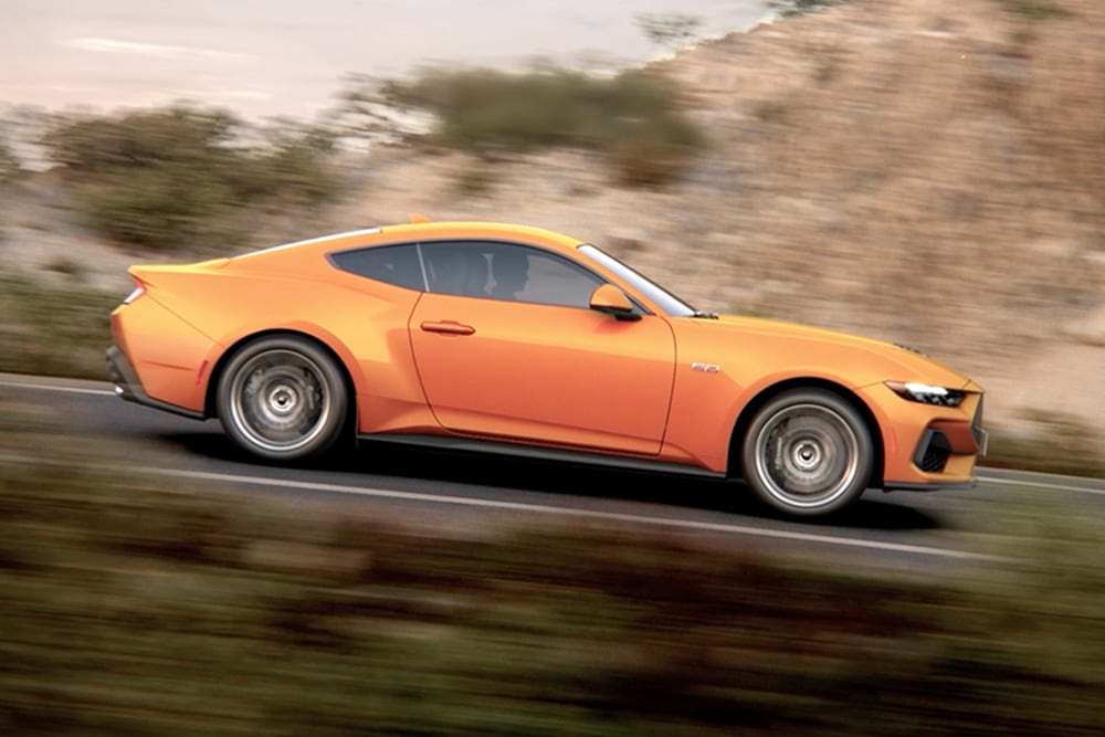 Widok z boku Ford Mustang GT Fastback w kolorze Orange Fury jadącego drogą