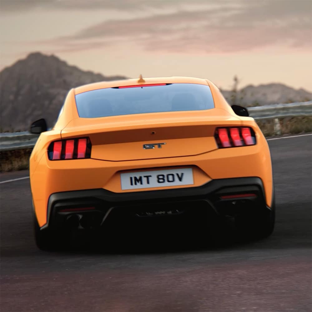 Tył Ford Mustang GT Fastback w kolorze Orange Fury pokonującego ostry zakręt na wiejskiej drodze
