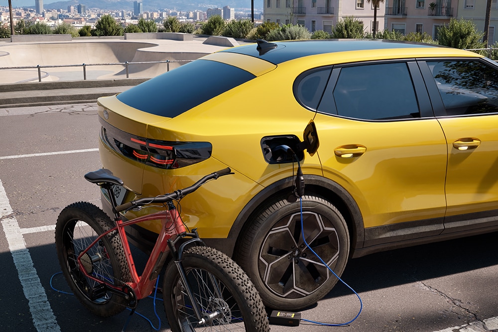 Żółty Ford Capri® podłączony do miejskiej ładowarki oraz stojący obok czerwony rower.