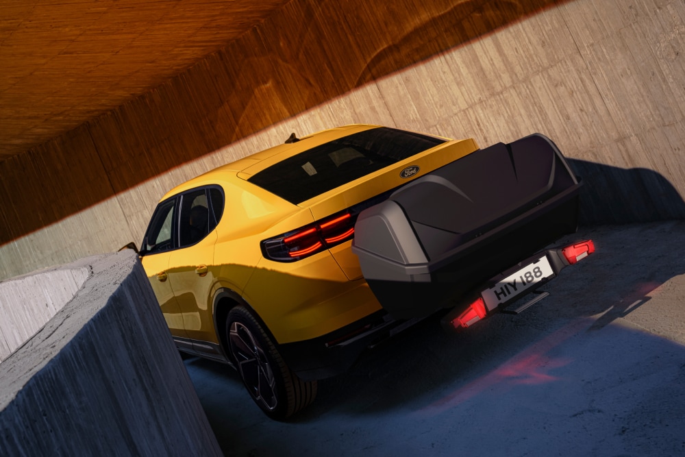 Żółty Ford Capri stojący na nowoczesnym betonowym parkingu, widok od tyłu pokazujący bagażnik przymocowany do tylnej części pojazdu.