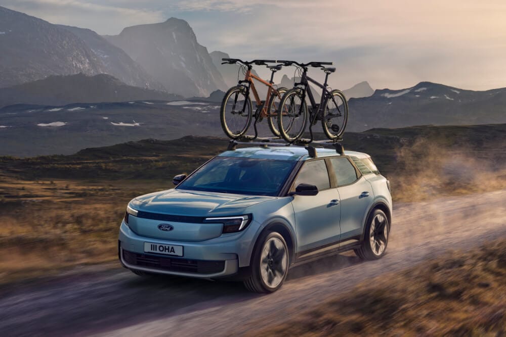 Niebieski Ford Explorer jadący po bezdrożach, z zamontowanym bagażnikiem rowerowym na dachu i dwoma przymocowanymi do niego rowerami.