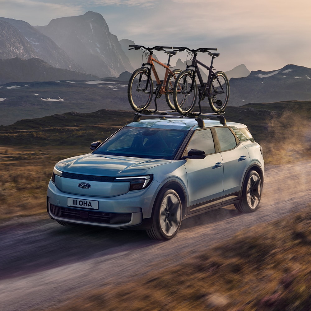 Niebieski Ford Explorer jadący po bezdrożach, z zamontowanym bagażnikiem rowerowym na dachu i dwoma przymocowanymi do niego rowerami.