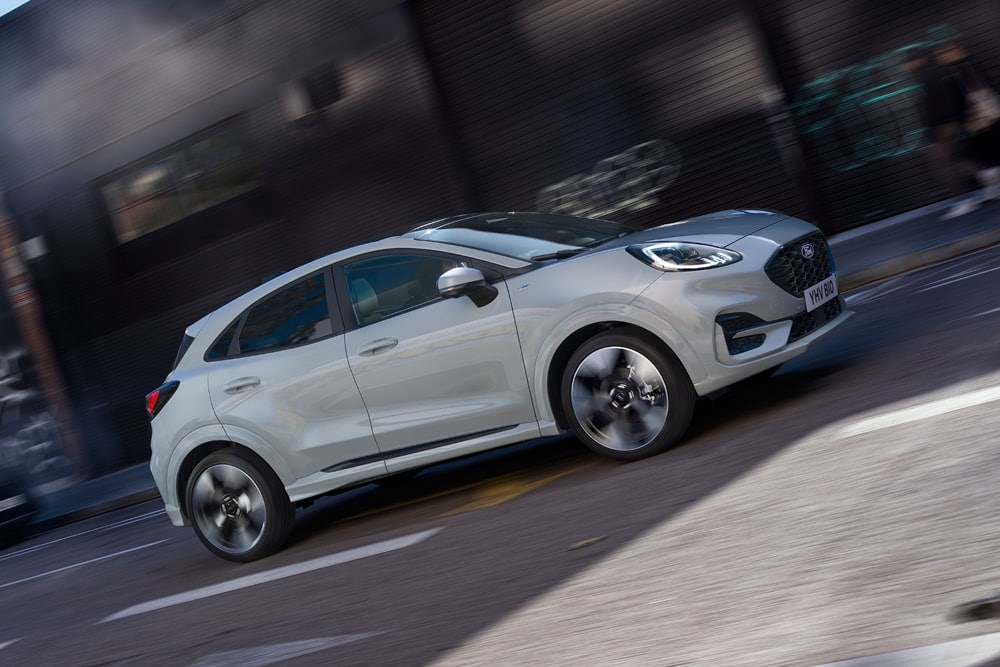 Srebrny Ford Puma z gamy kompaktowych miejskich SUV-ów Forda jadący miejską ulicą.