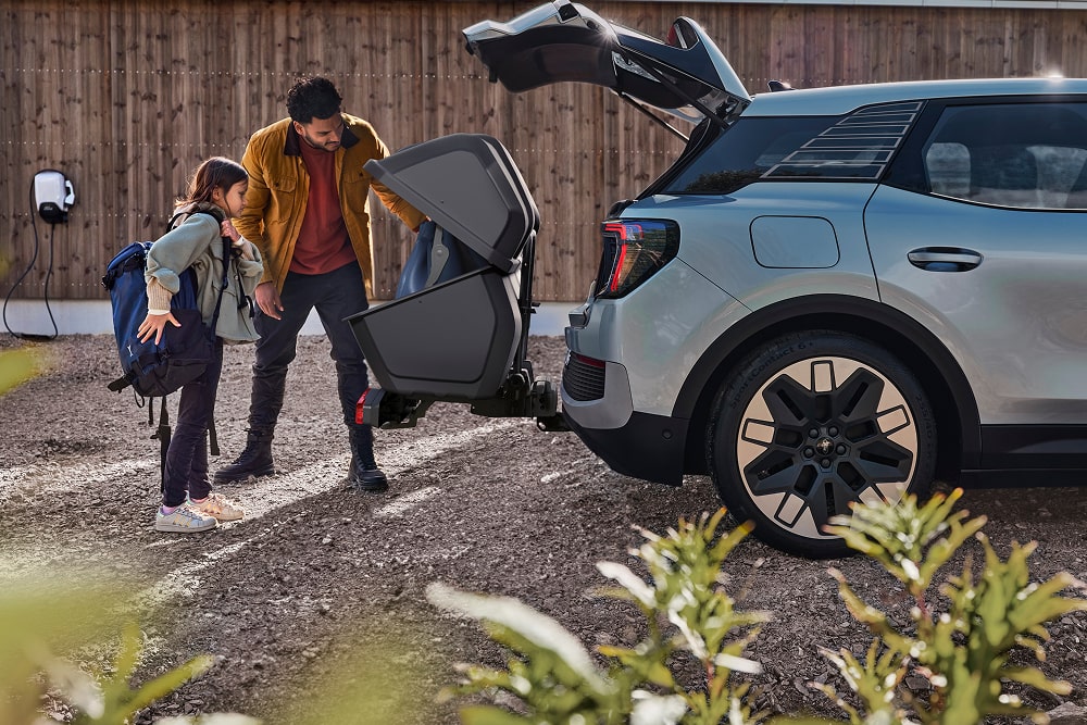 Mężczyzna z dzieckiem ładujący złożony wózek do otwartego bagażnika SUV-a Ford Explorer.