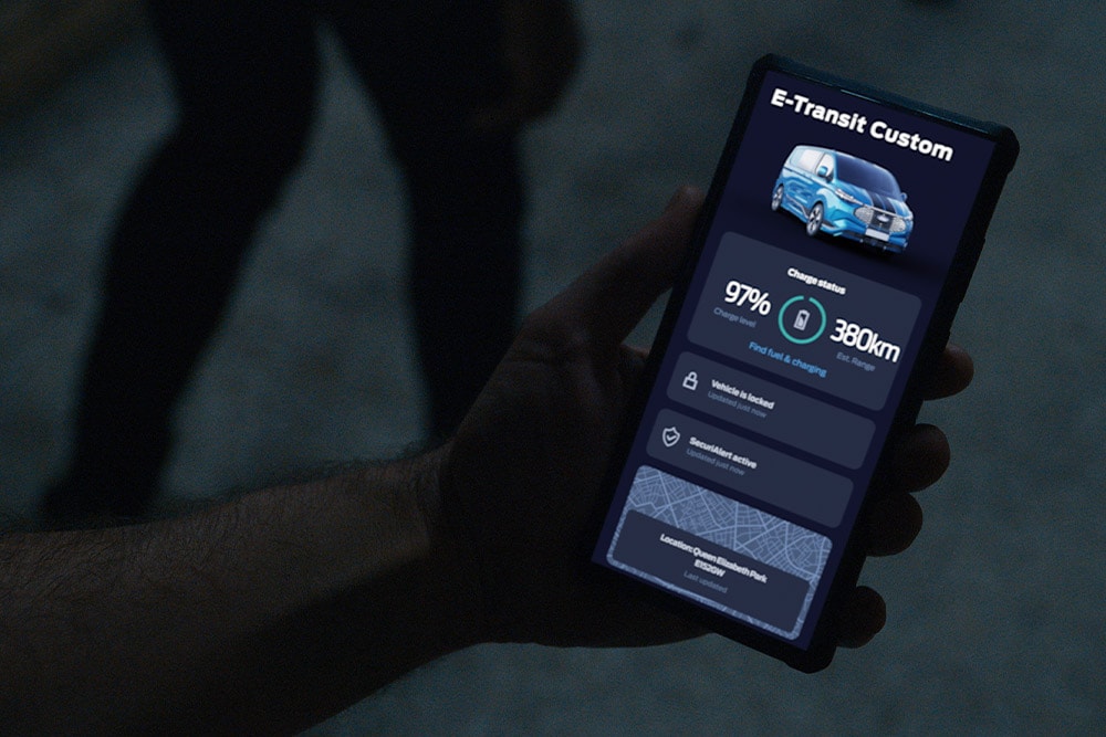Smartfon wyświetlający model E-Transit Custom w aplikacji FordPass, pokazujący stan naładowania pojazdu oraz jego lokalizację.