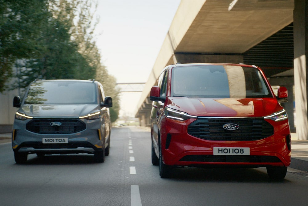 Szary i czerwony van Ford Transit Custom jadą autostradą.