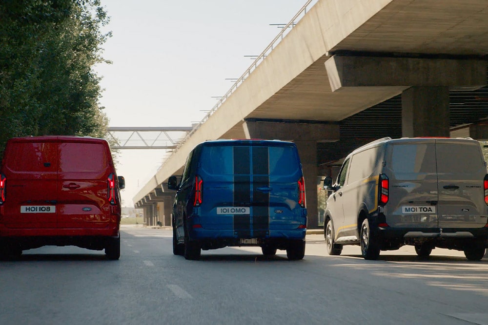 Trzy vany Ford Transit Custom jadące autostradą.