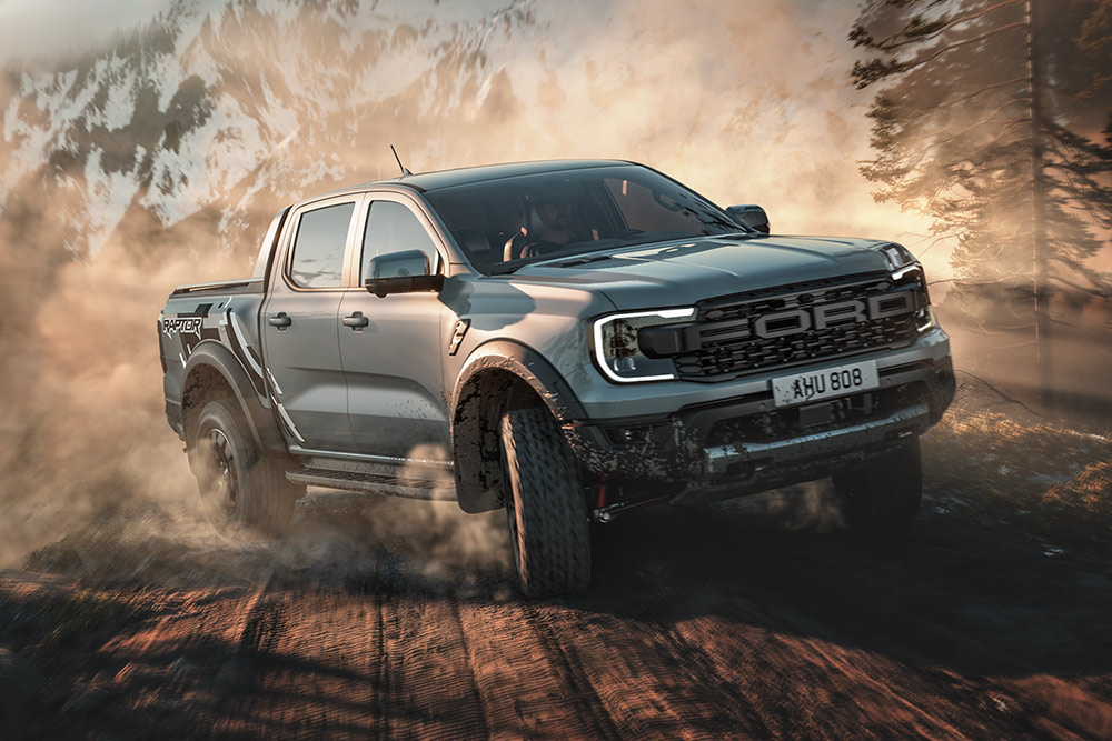 Ford Ranger Raptor w trybie Baja jadący nieutwardzoną drogą z górskim krajobrazem w tle.