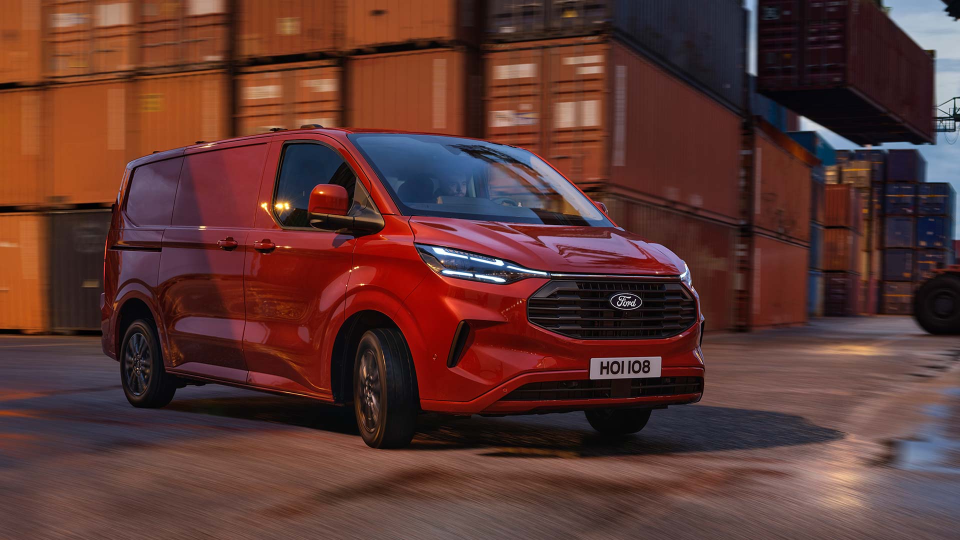 Czerwony van Ford Transit Custom przejeżdża przez teren stoczni. 