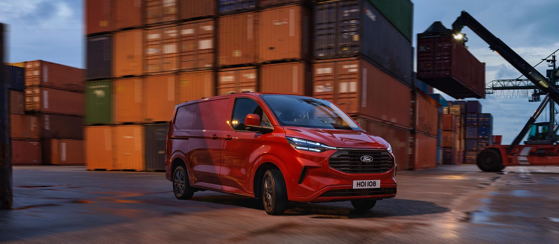 Czerwony van Ford Transit Custom przejeżdża przez teren stoczni.