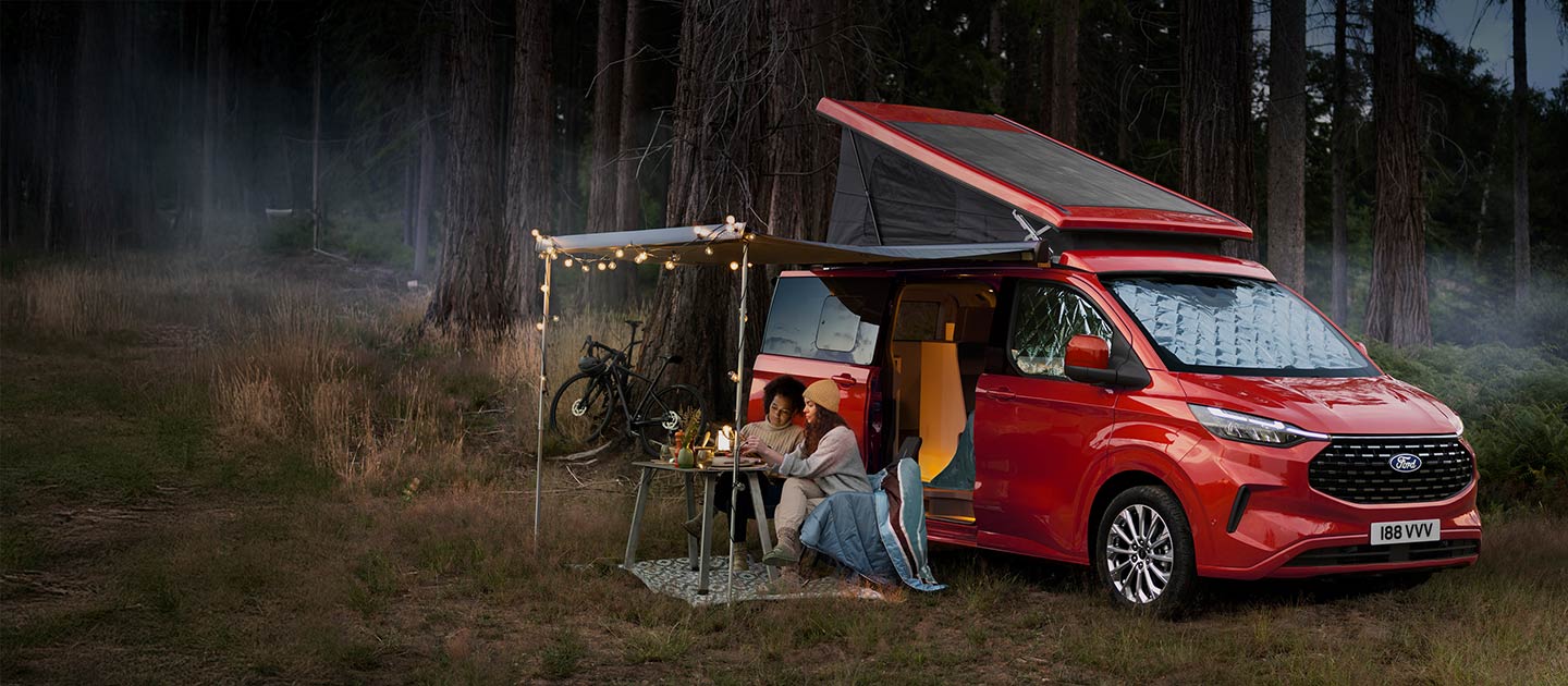 Czerwony kamper Ford Transit Custom Nugget zaparkowany w lesie.