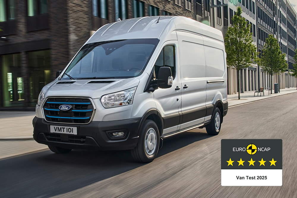 Srebrny elektryczny van Ford E-Transit jadący po drodze z odznaką „Gold 2022 Commercial Van Safety”.