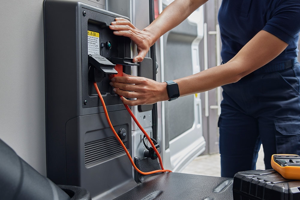 Zbliżenie na osobę podłączającą kabel ładujący wewnątrz elektrycznego vana Ford E-Transit.