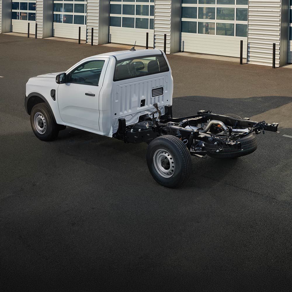 Biały Ford Ranger podwozie z kabiną stoi zaparkowany przed rzędem bram garażowych.