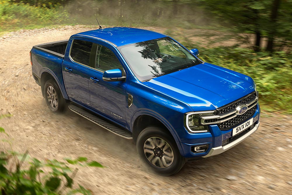 Niebieski pick-up Ford Ranger jedzie nieutwardzoną drogą przez las, zostawiając za sobą tuman kurzu.