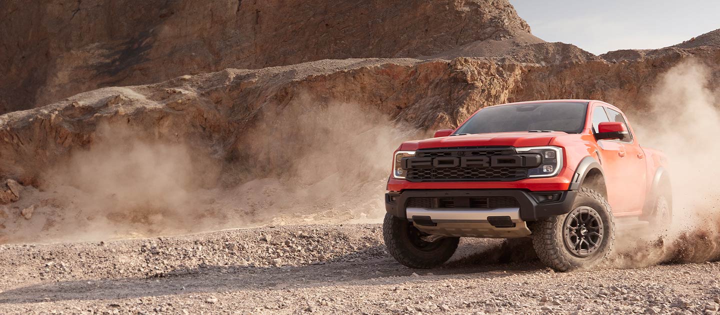 Czerwony Ford Ranger Raptor wznosi tumany kurzu, przejeżdżając przez pustynny krajobraz.