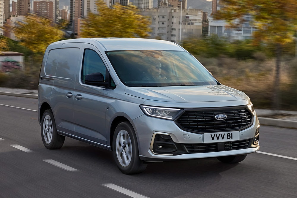 Ford Transit Connect jadący ulicami miasta, ze światłami przeciwmgielnymi z chromowaną oprawą oraz automatycznymi reflektorami.