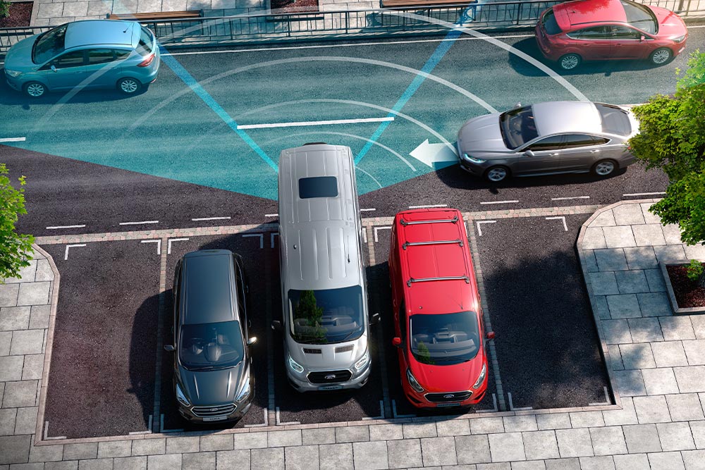 Cofający srebrny Ford Transit Van, widoczne niebieskie linie pomocnicze tylnego czujnika parkowania.