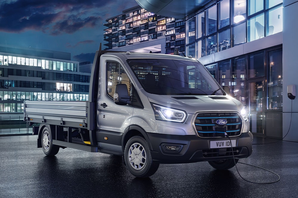 Srebrny Ford E-Transit w wersji podwozie z kabiną zaparkowany przed nowoczesnym budynkiem w nocy.