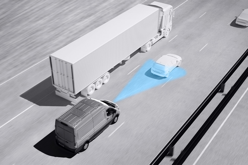 Szary van Ford Transit z niebieskimi liniami na drodze wskazującymi korzystanie z zaawansowanych systemów wspomagających kierowcę.